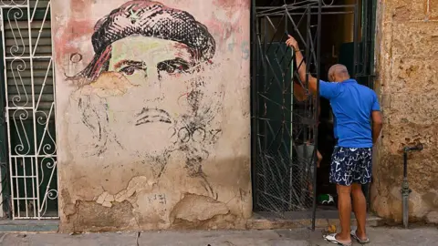 Getty Images A faded mural of Che Guevara on a wall with a man standing nearby in Cuba
