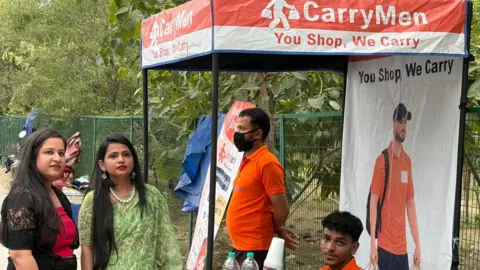 Geeta Pandey/BBC Founders Ritu Kandari Srivastava (in green sari) and Kanishka Malhotra (in black trousers and red top) at the CarryMen kiosk in Lajpat Nagar market