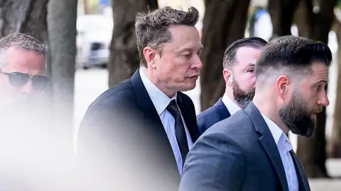 Getty Images Elon Musk, in a dark suit and tie with a crisp white shirt and pursed lips, arrives at federal court on March 4, 2026 in San Francisco, California. 