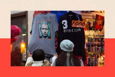 Bloomberg via Getty Images Two female shoppers wearing hats examine a grey t-shirt bearing the Time cover which is hanging outside a shop selling souvenirs