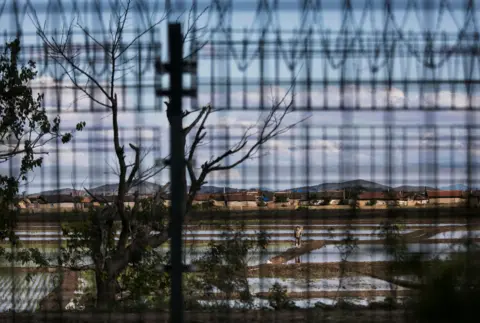 Getty Images A North Korean farmer is seen through a razor wire fence near the border city of Dandong, Liaoning province, northern China across from the city of Sinuiju, North Korea on May 23, 2017 in Dandong, China