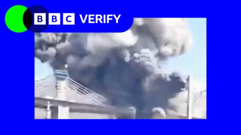 BBC Smoke rises from a strike on the B1 Bridge in Iran. The photo is imposed over the BBC Verify colours and branding. 