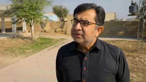 A man wearing glasses and a dark shirt looks to the left of the camera.