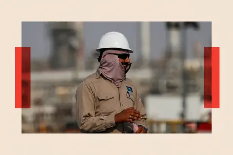 Reuters An oil rig worker wearing a white hard het and khaki boiler suit looks away from the camera