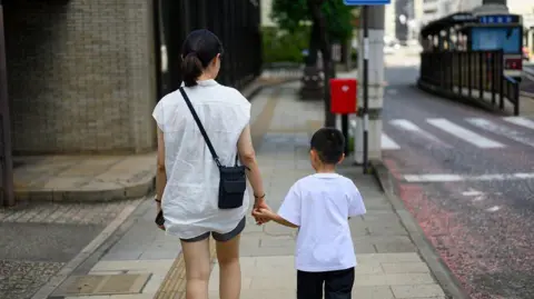 Getty Images Backview of a mother and her young son holding hands and walking down a street