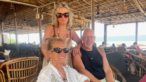Nikhil Inamdar Nicola (left), Alison (centre) and Dwayne - British tourists at a shack in Goa, smiling for the camera. 