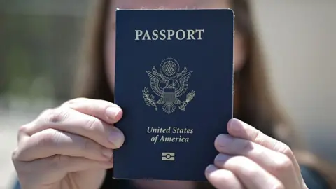 Getty Images A woman holds up her US passport, blocking her face with it.