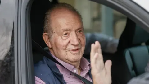 EPA Former King Juan Carlos waves with his right hand from a car to reporters after competing in a regatta in Sanxenxo, Spain in October 2023.