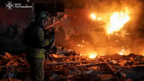 Reuters A firefighter works at the site of a building damaged during overnight Russian drone and missile strikes with flames seen in the background
