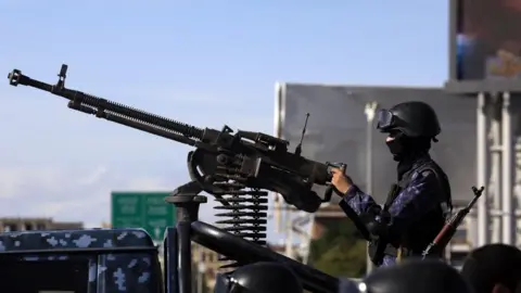 EPA A Houthi soldier in blue camouflage uniform, with a black helmet with goggles around it, a mask covering the lower part of his face and a gun slung on his left shoulder, mans a machine-gun during a pro-Iran event