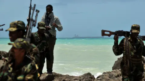 AFP via Getty Images Armed gunmen stand on a rocky base next to the shore in Somalia
