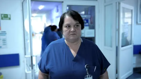 BBC Surgeon Dr Oana Goidescu on shift at Buzău Hospital in blue scrubs. She has mid length black hair