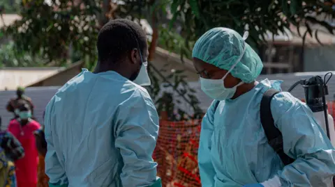 Anadolu via Getty Images Two health workers are pictured wearing blue protective gear