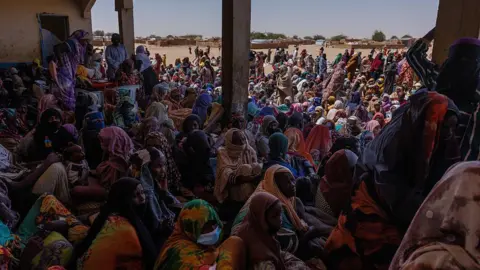 Getty Images Hundreds of refugees sitting under a shelter in Chad, overspilling outdoors