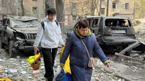 Reuters A man and woman carry bags past damaged vehicles as they evacuate following a Russian strike in Ukraine 