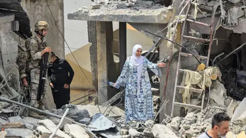 AFP A woman makes her way through the rubble as a Lebanese soldier looks on at the site of a residential building destroyed in an Israeli strike in the southern town of Burj al-Shamali, on the outskirts of Tyre, Lebanon (27 May 2026)