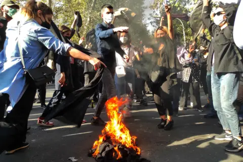 Getty Images Iranian protesters set their scarves on fire while marching down a street on October 1, 2022 in Tehran, Iran. 