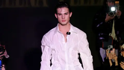 Victor VIRGILE/Gamma-Rapho via Getty Images Clavicular walking down a fashion runway wearing a white shirt. He has dark hair.