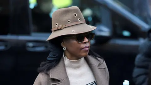Reuters Diezani Alison-Madueke outside Southwark Crown Court in January. She is wearing a brown hat, with matching brown coat and a jumper. She has sunglasses on and earrings.