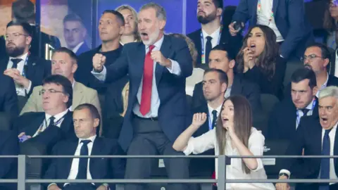 Getty Images King Felipe, wearing a suit and tie, stands as he cheers in a football stand surrounded by people