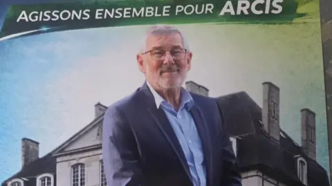 BBC An election poster shows a man with a blue jacket and shirt and a grey beard