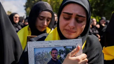Reuters A woman wearing a black hijab mourns a relative killed in an Israeli air strike, while clutching a portrait of the victim (22/04/26)