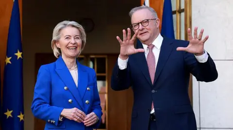 Getty A woman in a bright blue suit smiles next to a man in a dark blue suit who is gesturing with his hands.