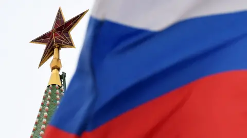 AFP via Getty Images A star on the top of a spire of the Kremlin is pictured with the Russia flag flying in the foreground showing Russian red, white and blue colours in an image taken in the Red Square in Moscow in 2018. 