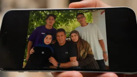 Neha Sharma/BBC A person holds a phone showing a photo of five members of a family who were killed in an Israeli air strike in Saksakiyeh, southern Lebanon