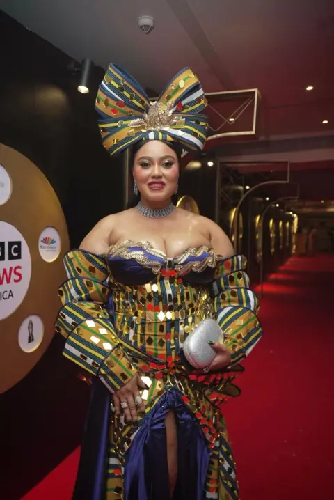 BBC/GIFT UFUOMA Reality TV star, OJ Posharella graces the red carpet with a giant bow sitting on her head as she stuns in her multi-layered colorful outfit she designed herself.