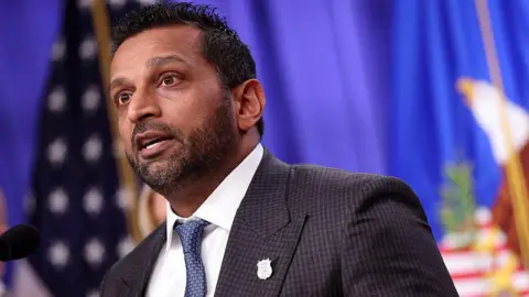 Getty Images close-up of Kash Patel speaking, wearing a suit and tie in front of American flag