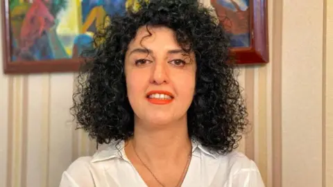 Reuters A woman with curly black hair dressed in a white collared shirt and red lipstick, smiles to the camera. 
