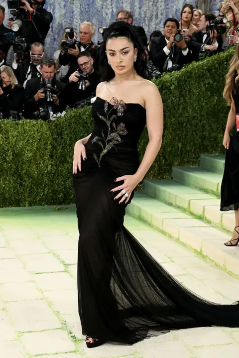 Getty Images Charlie XCX wears a black gown with a floral embellishment on the front.
