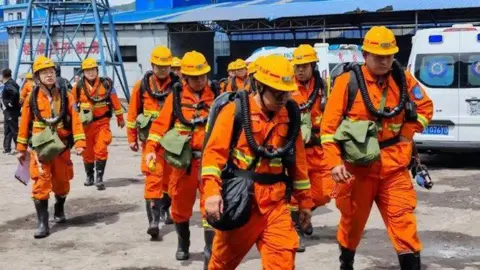 Xinhua Rescuers in orange safety suits and helmets walking near industrial buildings
