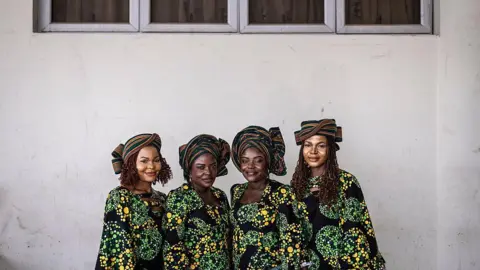 AFP via Getty Images Twin sisters Taiwo and Kehinde Oketikun pose for a photograph with twin sisters Taiwo and Kehinde Adisa. All four wear matching multi-coloured outfits.
