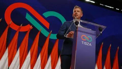 Léa Guedj/BBC A man stands at a podium