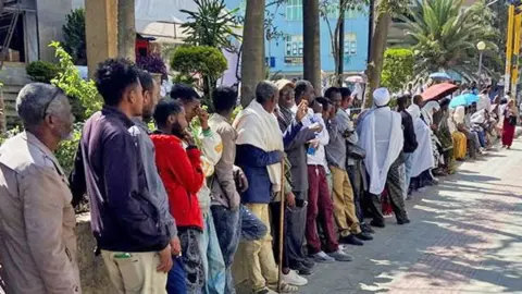 Reuters A long line of men and women queuing along a street in Mekelle for the bank - January 2026