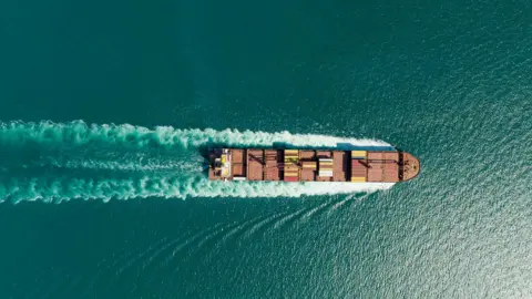 Getty Images An aerial view of a container ship on a blue-green sea.