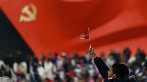 Getty Images A little boy raises a small flag at the plaza of the Museum of the Communist Party of China in Beijing. The foreground is blurred, but one can make out a sculptural flag of the Communist Party in the background