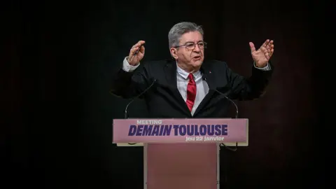Getty Images Leader of far-left party, La France Insoumise Jean-Luc Mélenchon before a podium reading "Meeting, DEMAIN TOULOUSE (tomorrow Toulouse), Jeu 22 janvier". He is speaking animatedly 