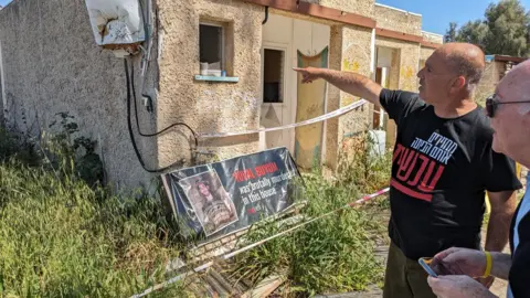 A man points at a burnt house on a kibbutz which was attacked on 7 October 2023