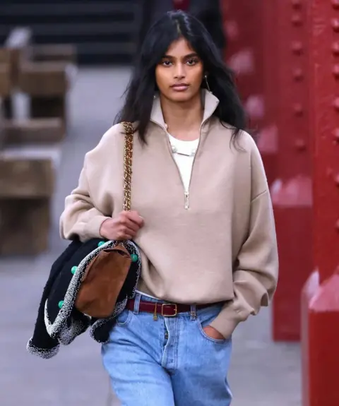 Bhavitha Mandava/Instagram Bhavitha wearing a white T-shirt, a half-zipped knit and loose jeans, with a brown leather purse for Chanel's Métiers d'Art show in New York.