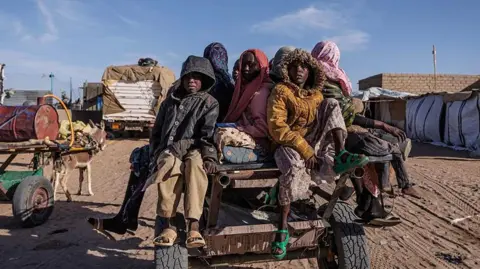 Getty Images Newly arrived Sudanese refugees sitting atop a cart prepare to ride back to their temporary shelter after receiving food aid in Chad