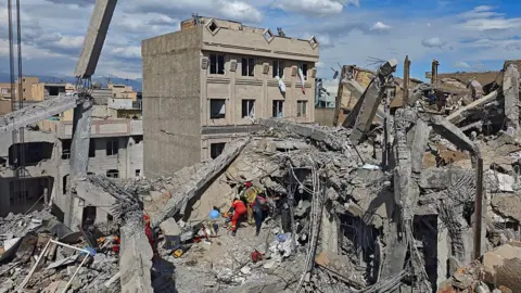 Getty Images Rescue workers search through the rubble of a building in Tehran, Iran, following an overnight strike. Photo: 28 February 2026. 
