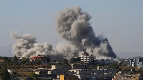 Reuters Long shot of a large grey cloud of smoke billowing over a town with some five-storey buildings in southern Lebanon after an Israeli strike.