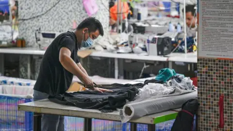 Getty Images A worker holding a pair of large scissors while producing clothes at a Guangzhou textile factory that supplies clothes to fast fashion e-commerce company Shein 