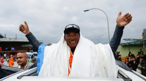 Getty Images Kami Rita Sherpa waves to supporters from the top of car after arriving back at base camp after his 28th climb in 2023