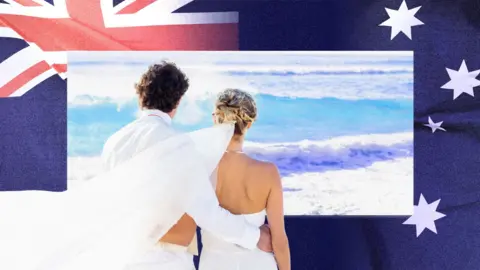 BBC A newlywed couple are seen looking out to sea on a beach, with a photo of the Australian flag in the background. 