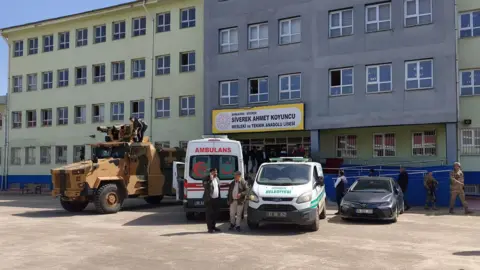 Reuters An armoured police vehicle, an ambulance and a vehicle for transporting bodies are parked at the entrance of a school