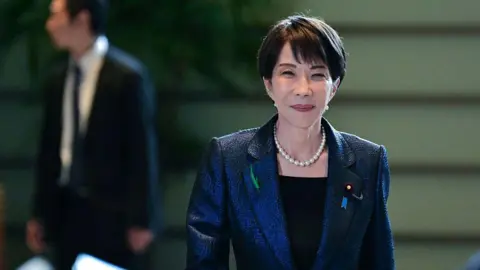 AFP via Getty Images Sanae Takaichi smiling and walking, while wearing a navy blazer